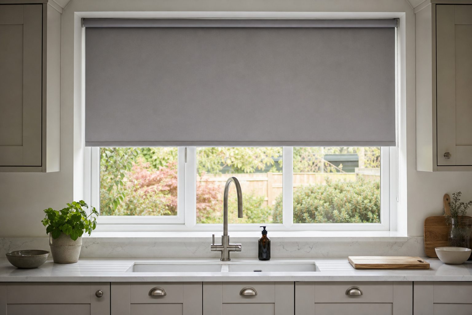 Grey made-to-measure roller blind half lowered over a kitchen sink window
